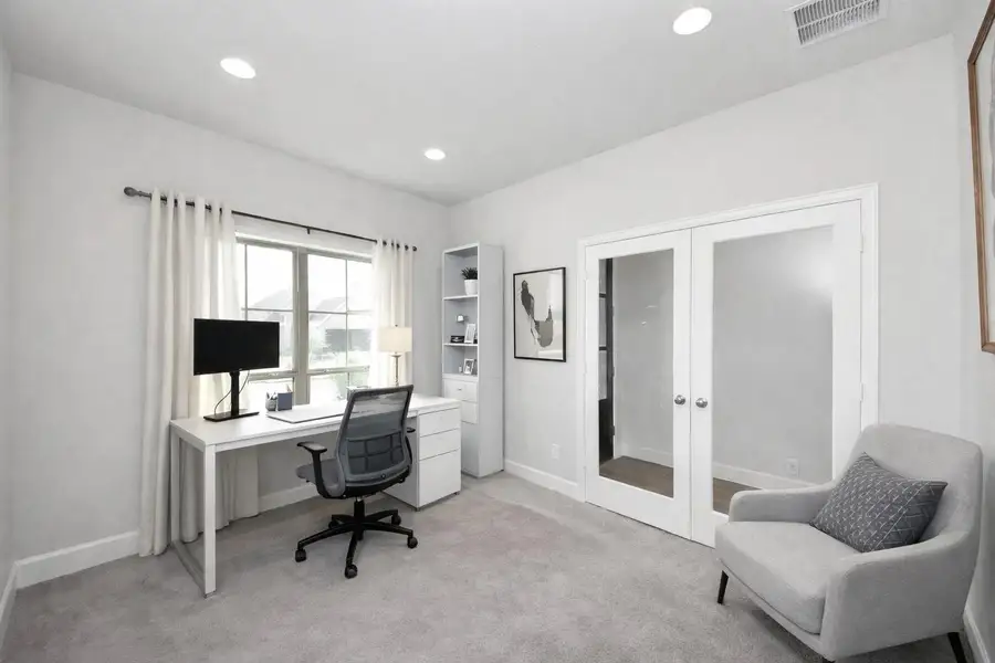 This bright home office features comfortable carpeted flooring, recessed lighting, and a desk positioned to enjoy views of the outdoors. Elegant French doors open to an adjoining room, creating a spacious and inspiring workspace ideal for productivity.