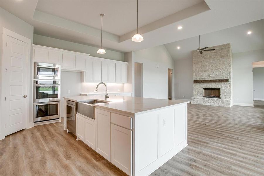 Kitchen with an island with sink, sink, a tray ceiling, and light hardwood / wood-style flooring