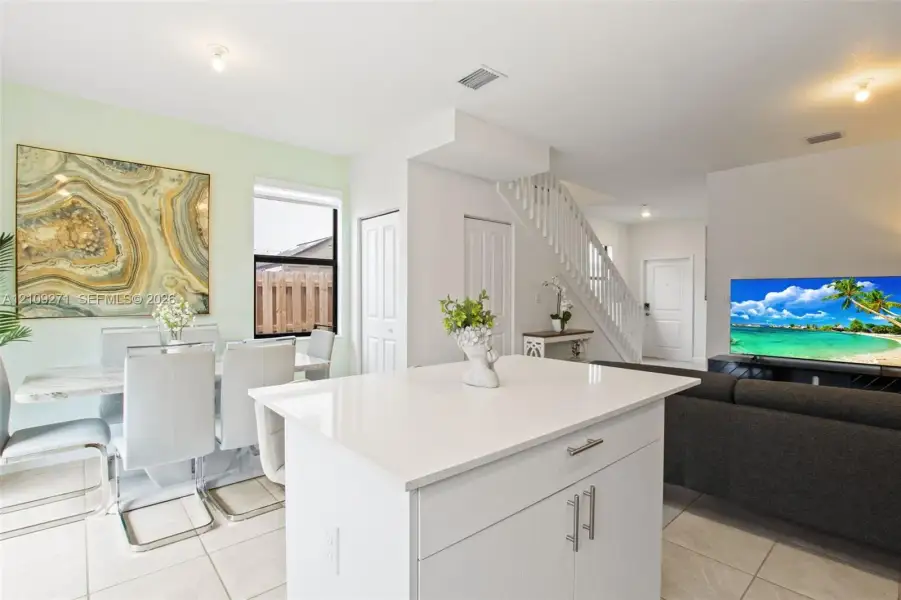 Kitchen featuring a central island with a quartz countertop, white cabinetry, light tile flooring, and a staircase with a white wood balustrade