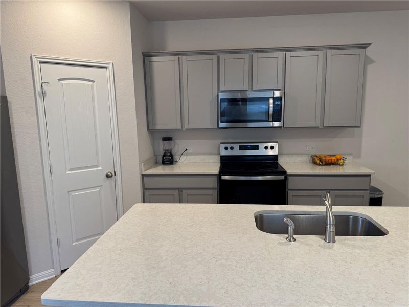 Kitchen with gray cabinets, stainless steel appliances, light stone countertops, and wood finished floors