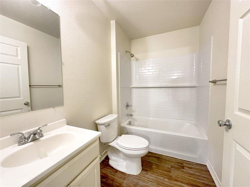 Full bath featuring dark wood-type flooring, a textured wall, shower / washtub combination, and vanity