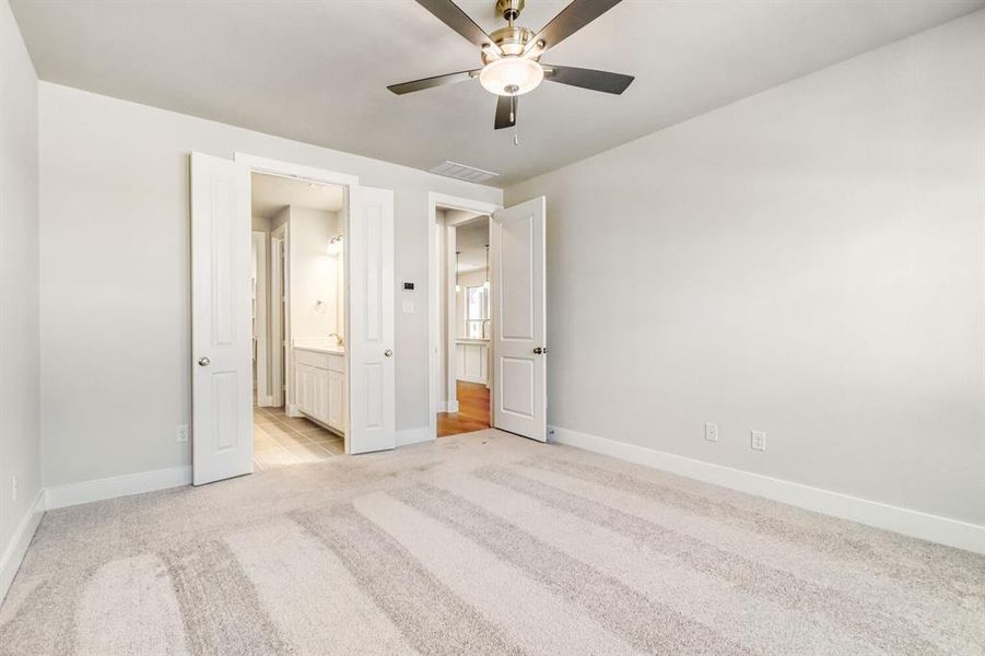 Unfurnished bedroom featuring light carpet, ceiling fan, and connected bathroom
