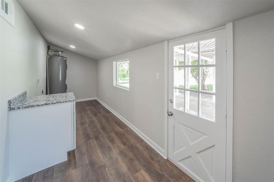 Laundry featuring dark wood-type flooring, light stone counters, water heater, and vaulted ceiling