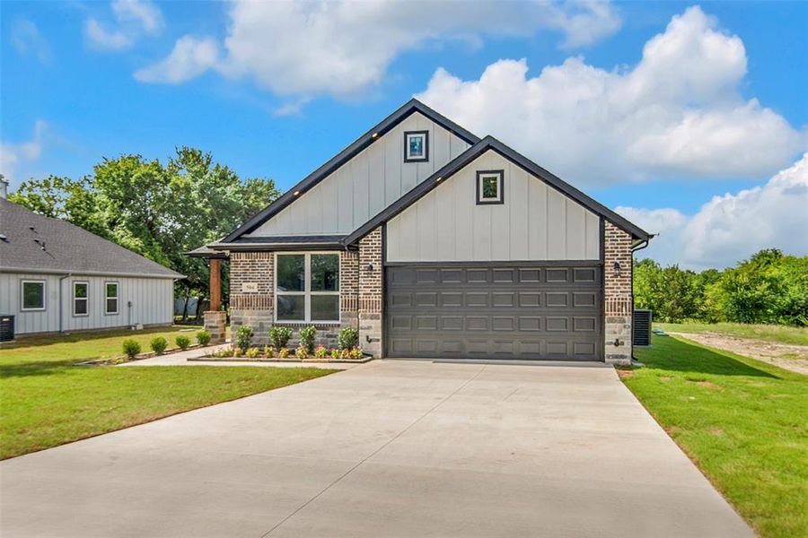 Modern farmhouse with concrete driveway, board and batten siding, a front yard, and brick siding Modern farmhouse with concrete driveway, board and batten siding, a front yard, and brick siding