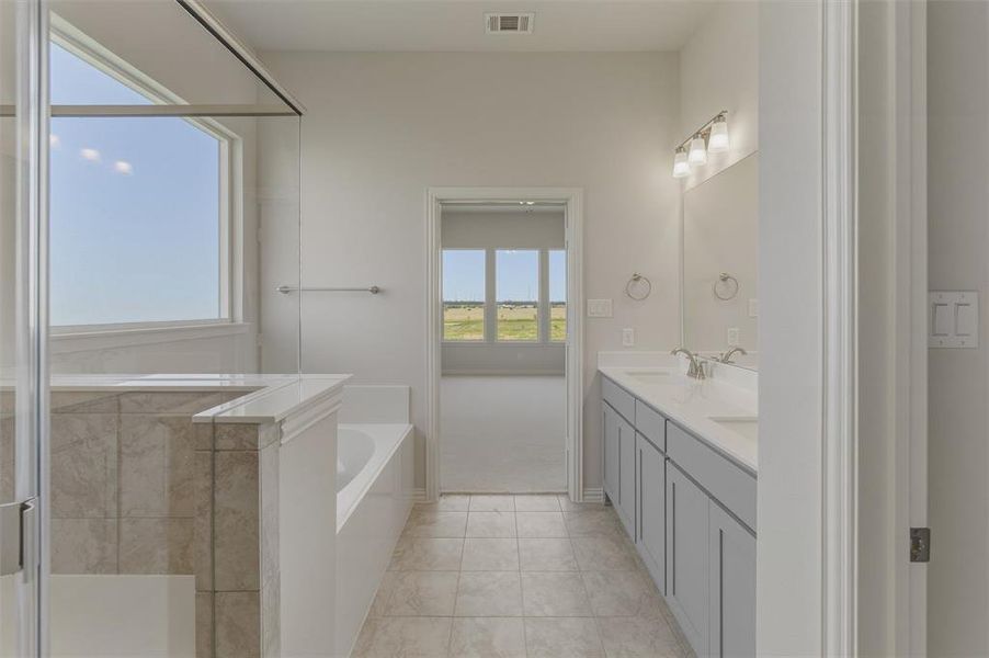 Contemporary bathroom featuring a spacious walk-in shower with clear glass enclosure, a white soaking tub, and a dual vanity with light gray cabinetry and white countertops