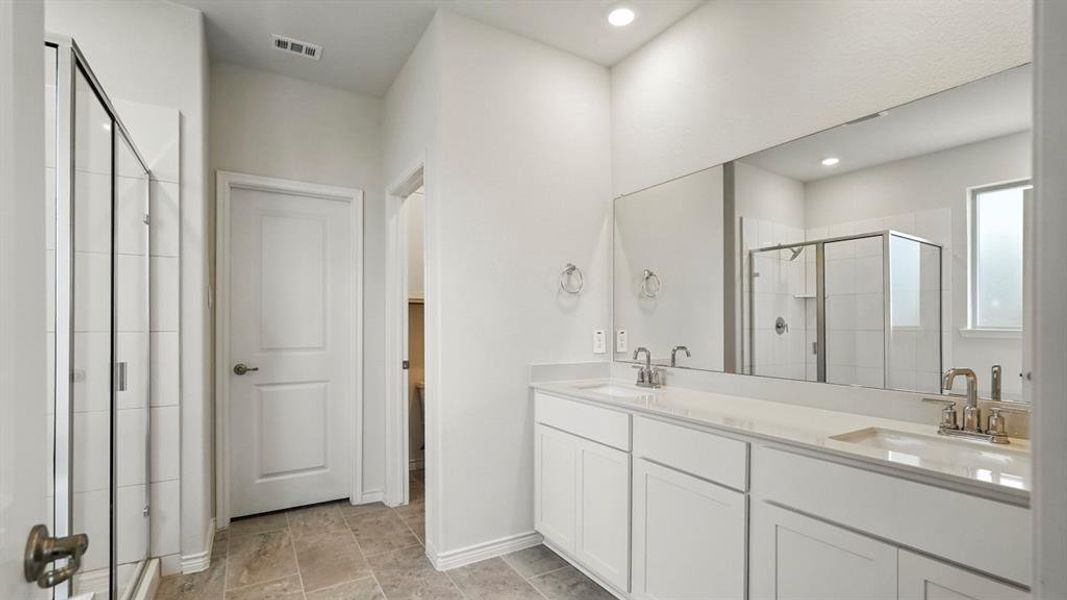 Bathroom featuring a dual vanity with white cabinetry, light-toned countertops, and brushed nickel fixtures Bathroom featuring a dual vanity with white cabinetry, light-toned countertops, and brushed nickel fixtures