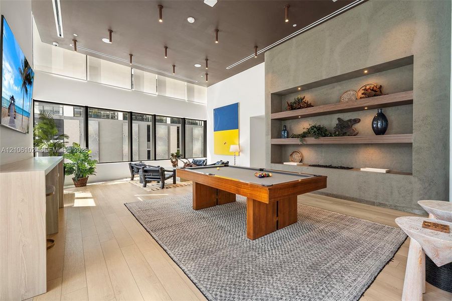 High-ceilinged room featuring wood-finish flooring, floor-to-ceiling windows, recessed architectural shelving, and custom ceiling-mounted accent lighting