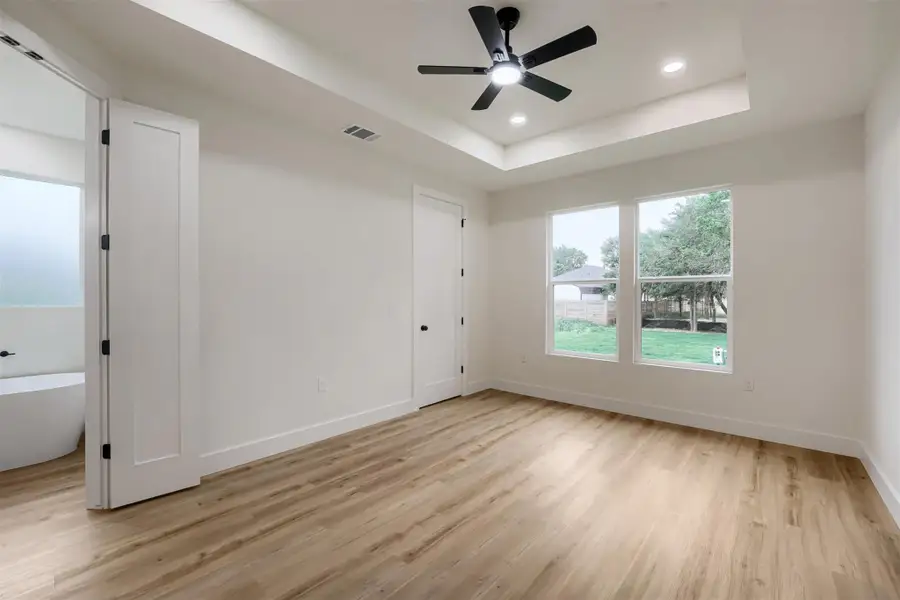 Spacious bedroom featuring wood-finish flooring, a tray ceiling with recessed lighting, and a modern ceiling fan