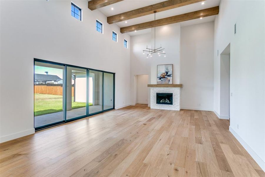 Unfurnished living room with a towering ceiling, beam ceiling, a chandelier, light wood-style floors, and a stone fireplace