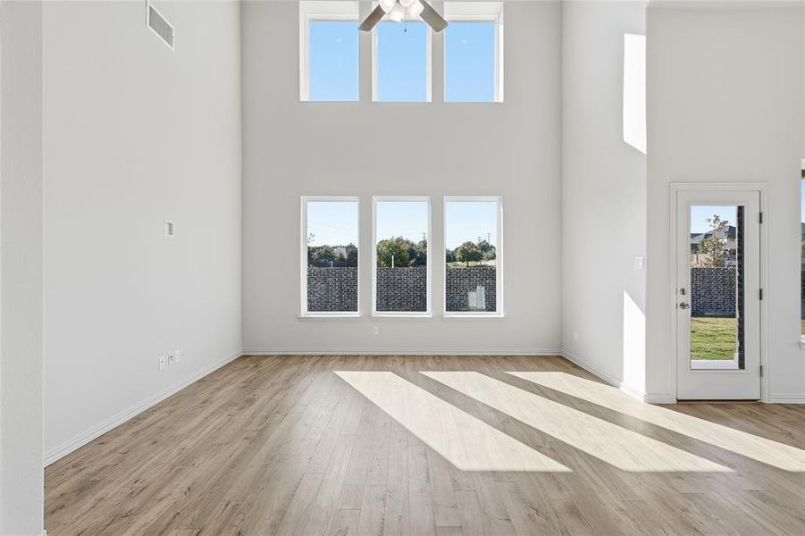 Unfurnished living room with healthy amount of natural light, light wood-style floors, ceiling fan, and a towering ceiling