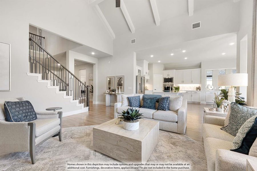 Open-concept living room with vaulted beamed ceiling, staircase, and kitchen visible in background
