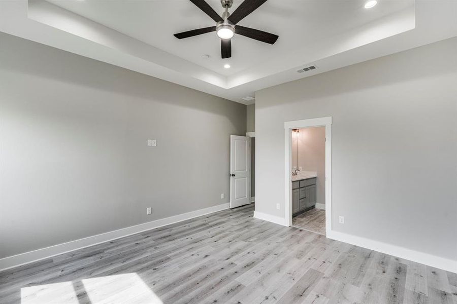 Unfurnished bedroom featuring light hardwood / wood-style floors, connected bathroom, ceiling fan, and a raised ceiling