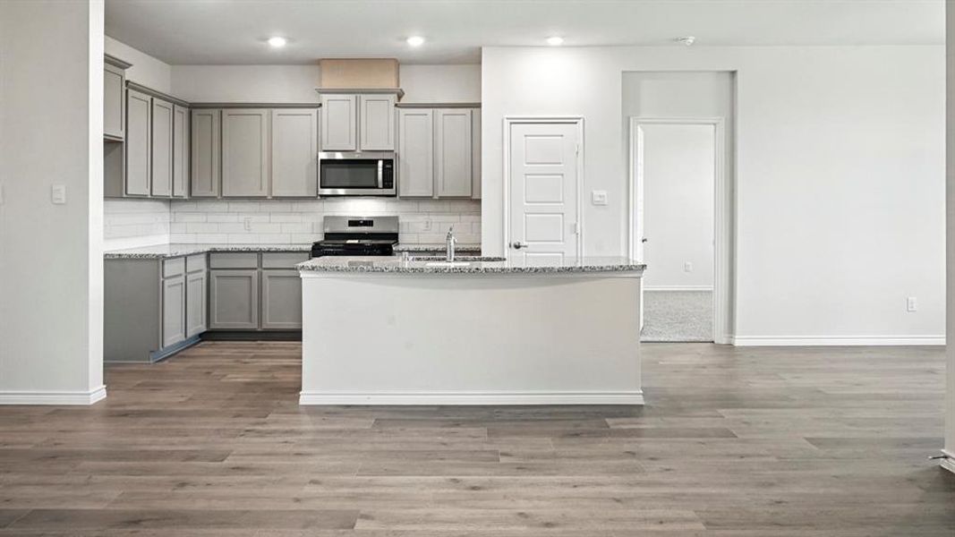 Contemporary kitchen featuring light gray cabinetry, stainless steel appliances, white subway tile backsplash, and speckled countertops
