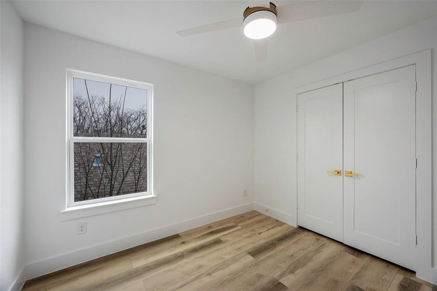 Unfurnished bedroom with ceiling fan, a closet, multiple windows, and light wood-type flooring