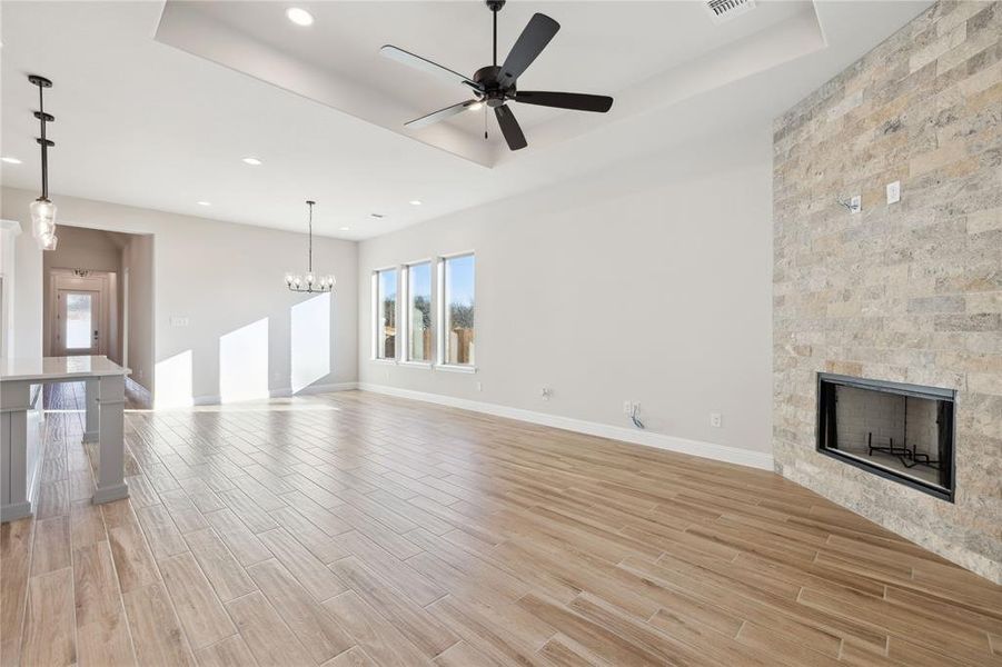 Unfurnished living room with a raised ceiling, a large fireplace, and ceiling fan with notable chandelier