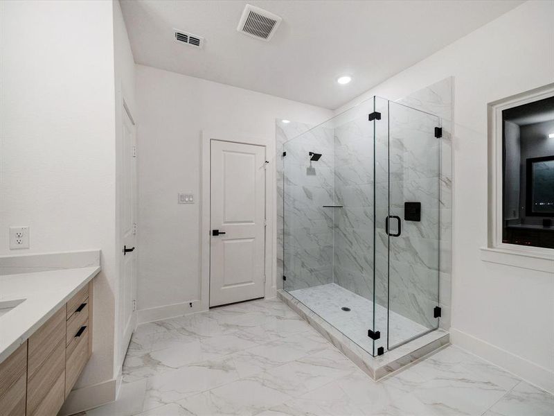 Full bathroom with a marble finish shower, vanity, and light marble finish flooring Full bathroom with a marble finish shower, vanity, and light marble finish flooring