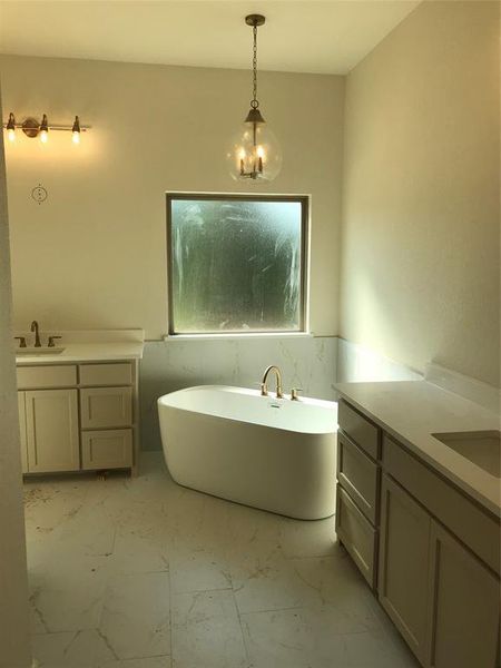 Bathroom featuring two vanities, a freestanding tub, light marble finish flooring, wainscoting, and tile walls