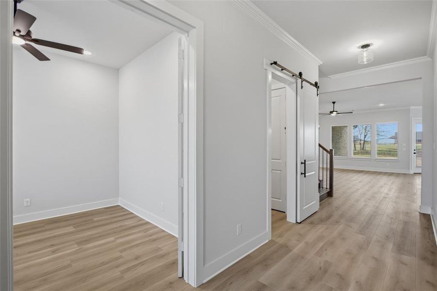 Hallway featuring a barn door, light wood-type flooring, crown molding, and recessed lighting