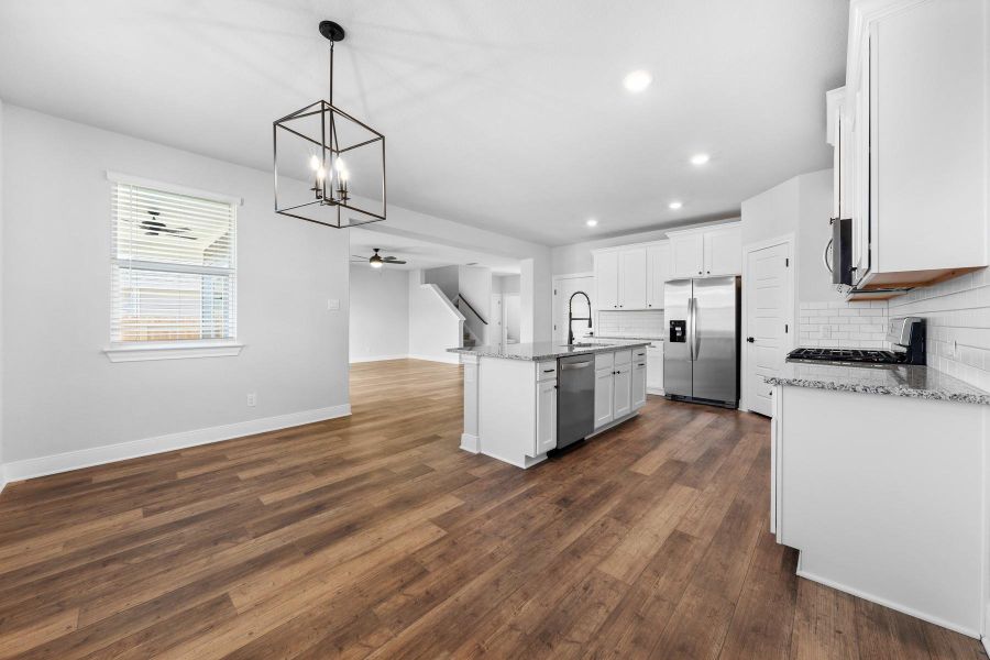 Kitchen with a chandelier, white cabinets, light stone countertops, a kitchen island with sink, and stainless steel appliances