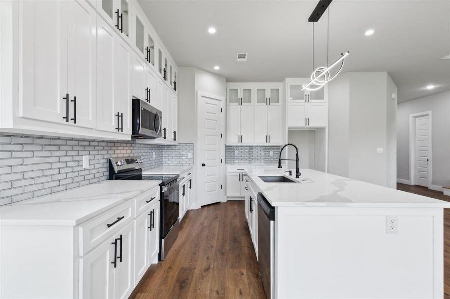 Kitchen featuring appliances with stainless steel finishes, white cabinetry, a kitchen island with sink, and sink