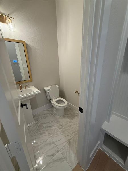 Half bathroom featuring toilet and light marble finish floors Half bathroom featuring toilet and light marble finish floors