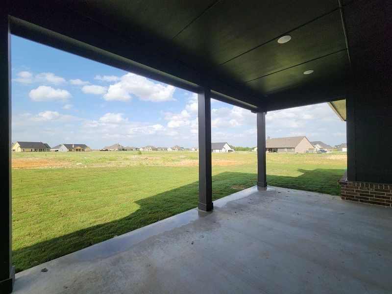 Covered patio with integrated recessed lighting, supported by dark-toned columns, offering an expansive grassy area