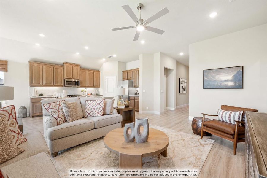 Open-concept living room with ceiling fan and hardwood floors, open to kitchen with wood cabinets in background