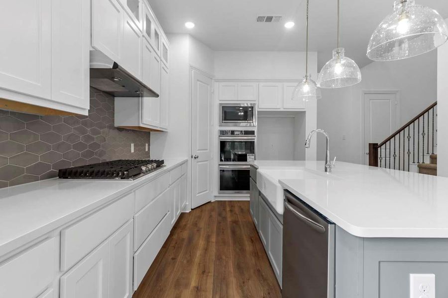 Kitchen with decorative backsplash, white cabinets, hanging light fixtures, stainless steel appliances, and dark wood-style floors Kitchen with decorative backsplash, white cabinets, hanging light fixtures, stainless steel appliances, and dark wood-style floors