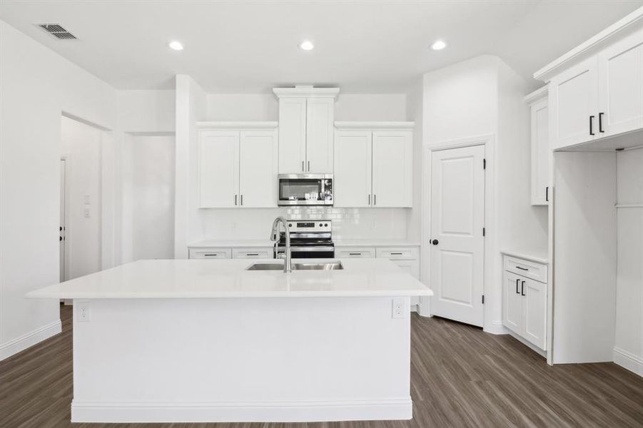 Kitchen featuring appliances with stainless steel finishes, dark hardwood / wood-style floors, an island with sink, and white cabinets