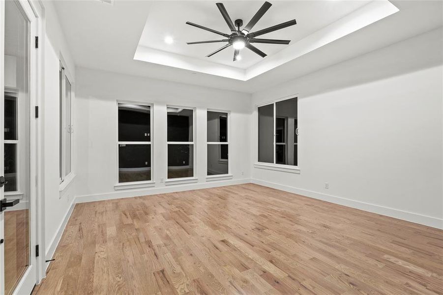 Empty room with light wood finished floors, recessed lighting, a raised ceiling, a ceiling fan, and baseboards