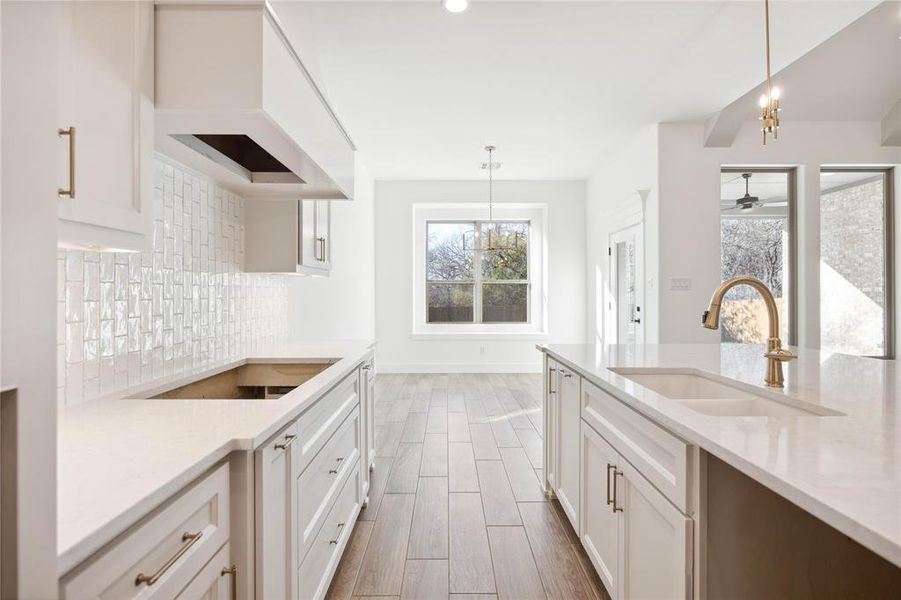 Kitchen featuring pendant lighting, backsplash, premium range hood, and sink