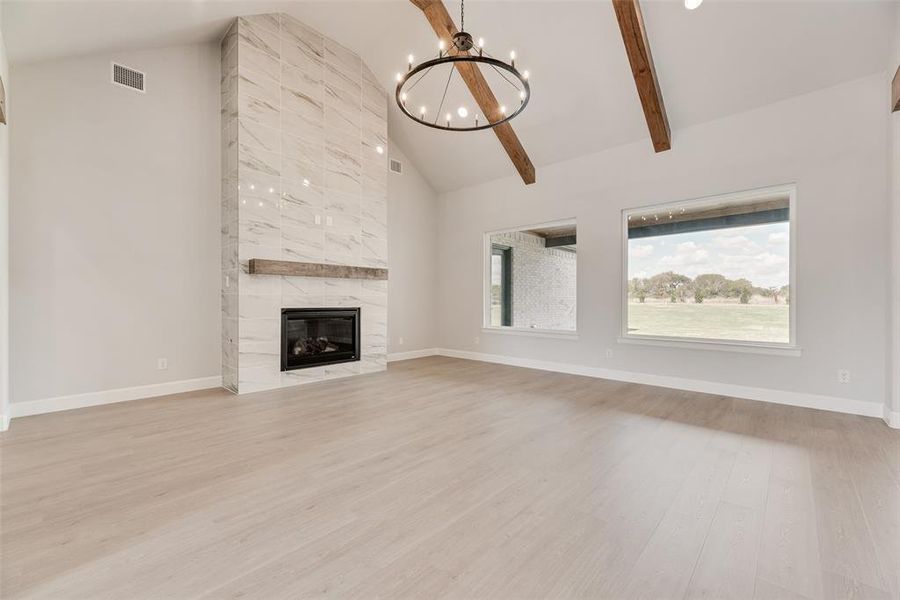 Unfurnished living room featuring high vaulted ceiling, a chandelier, light wood-type flooring, a fireplace, and beamed ceiling