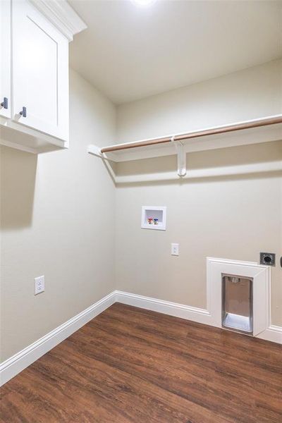 Laundry room with wood-finish flooring, light neutral wall paint, white baseboards, and overhead white cabinetry with dark hardware
