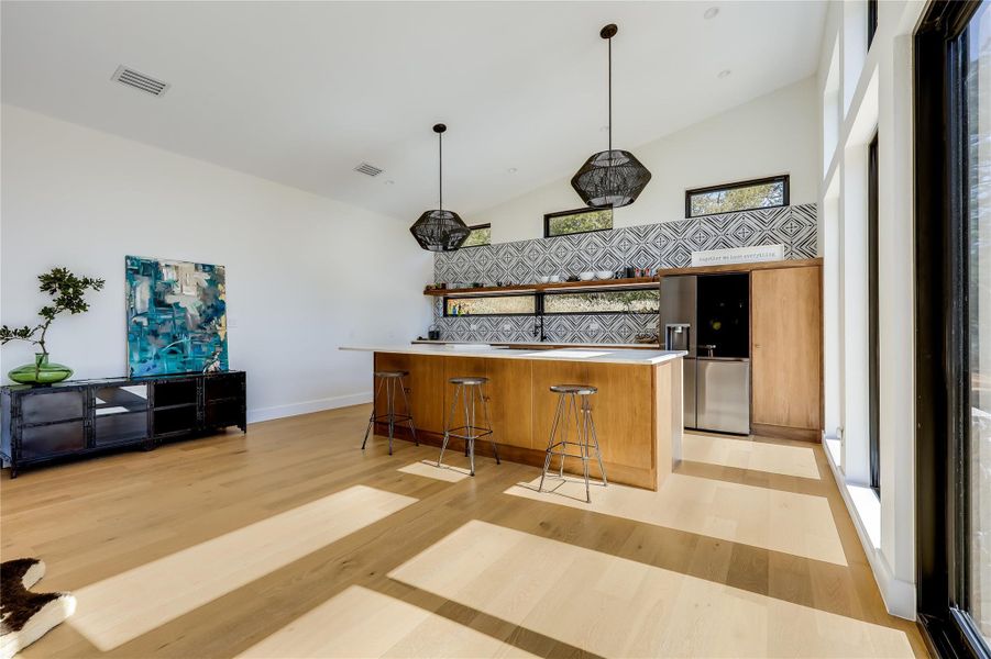 Kitchen featuring open shelves, stainless steel fridge with ice dispenser, light countertops, high vaulted ceiling, and brown cabinets