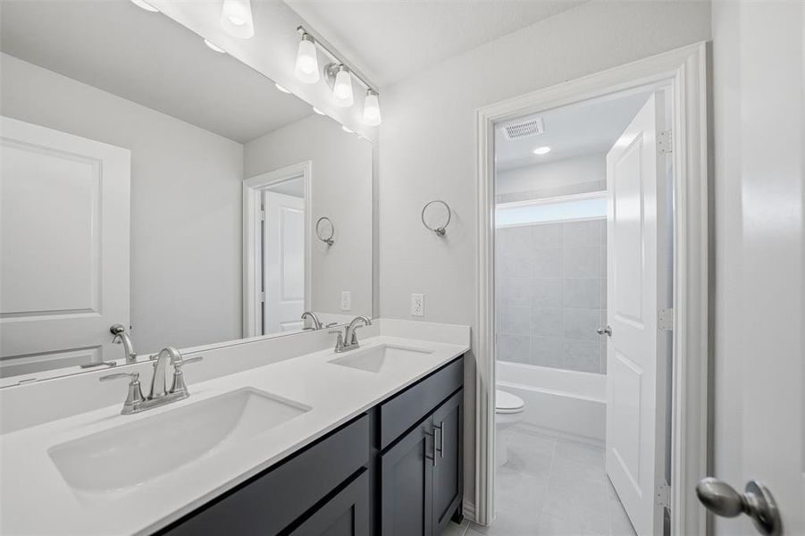 Bathroom featuring double vanity, shower / washtub combination, and light tile patterned floors Bathroom featuring double vanity, shower / washtub combination, and light tile patterned floors