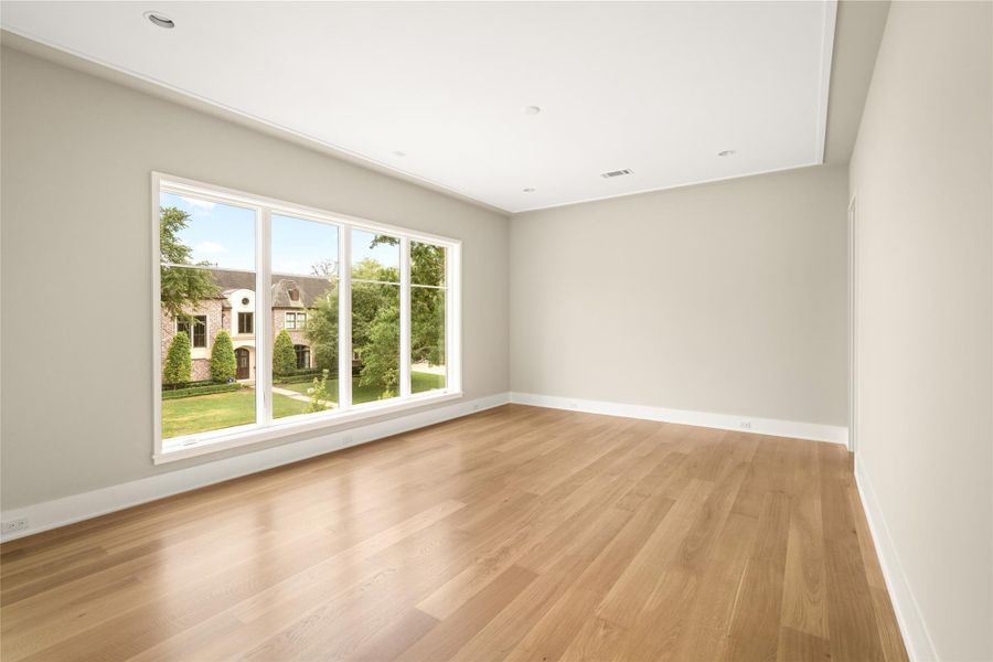 Spacious secondary bedroom with the continuation of wide-plank hardwoods seen throughout the home and a wall of windows overlooking the front grounds.