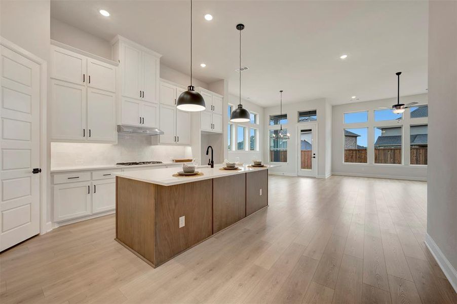Two tone kitchen featuring an island with sink, light wood-style flooring, two tone cabinetry, decorative light fixtures, and backsplash