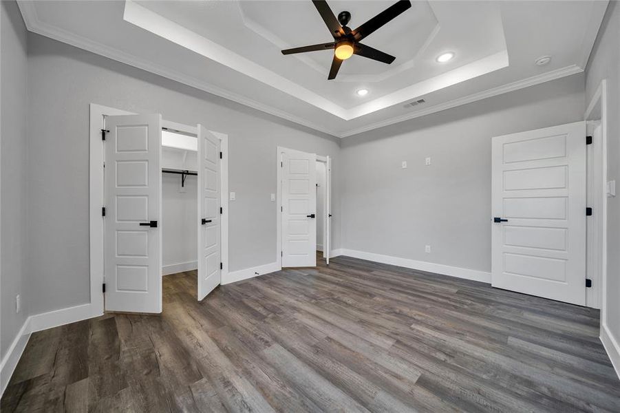 Unfurnished bedroom with ceiling fan, dark hardwood / wood-style floors, a spacious closet, a tray ceiling, and crown molding