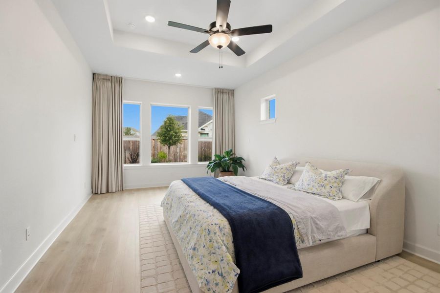 Spacious bedroom with large windows allowing natural light to flood the room, a cozy bed adorned with floral accents, and a modern ceiling fan for added comfort.