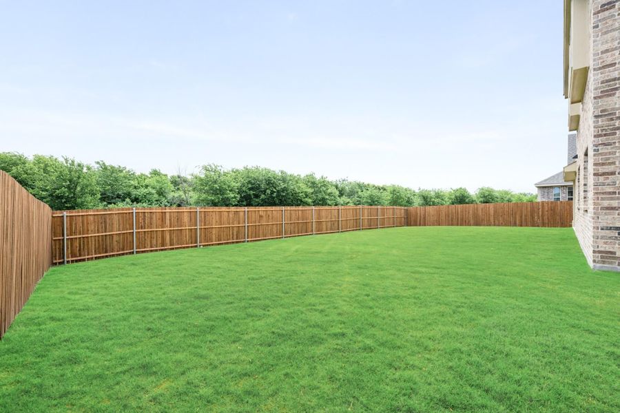 Large backyard with green grass lawn, wood privacy fence, and brick home exterior visible on right. Large backyard with green grass lawn, wood privacy fence, and brick home exterior visible on right.