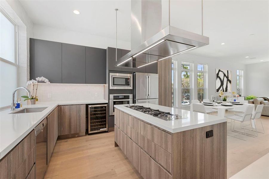 Kitchen with light wood-type flooring, stainless steel appliances, wine fridge, sink, linear gas range and modern vent hood