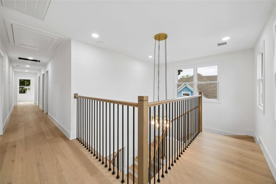 The upper-level landing overlooks the main staircase while creating connection between the secondary bedrooms and surrounding living spaces. Modern railing details, engineered wood flooring, and natural light carried through the hallway continue the home’s contemporary architectural consistency across both levels.