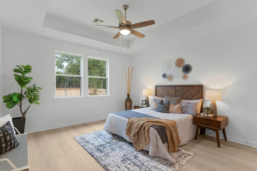 Bedroom with a raised ceiling, light wood-style flooring, baseboards, and a ceiling fan