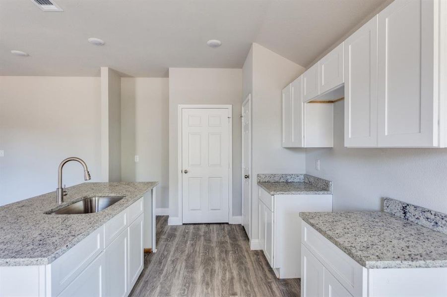 Kitchen with white cabinetry, wood finished floors, light stone countertops, and a center island with sink