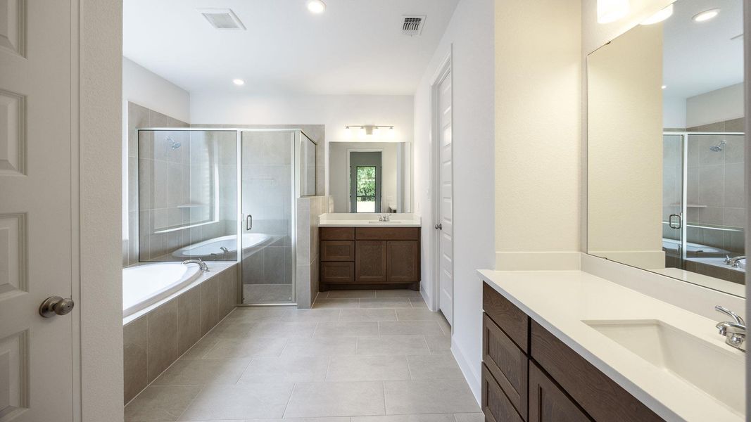 Full bath with a garden tub, a stall shower, two vanities, light tile patterned floors, and recessed lighting