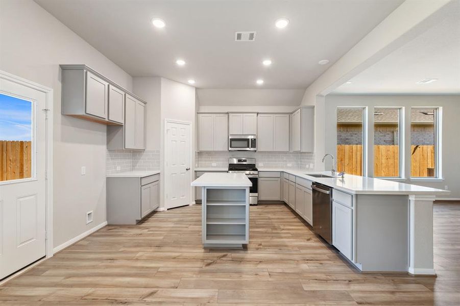 This light and bright kitchen features a large quartz island, white cabinets, a large sink overlooking your family room, recessed lighting, and beautiful backsplash.