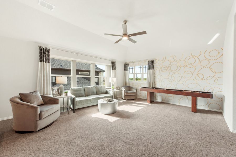 Spacious game room with carpet, ceiling fan, seating area, and shuffleboard table against a decorative accent wall