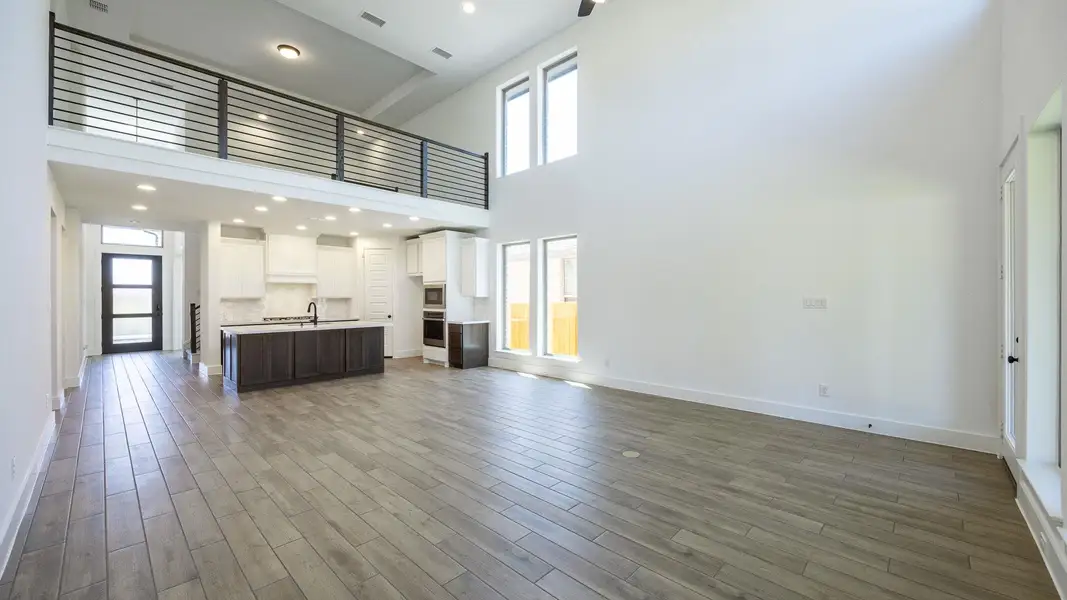 Unfurnished living room featuring baseboards, a high ceiling, visible vents, a sink, and wood finished floors Unfurnished living room featuring baseboards, a high ceiling, visible vents, a sink, and wood finished floors