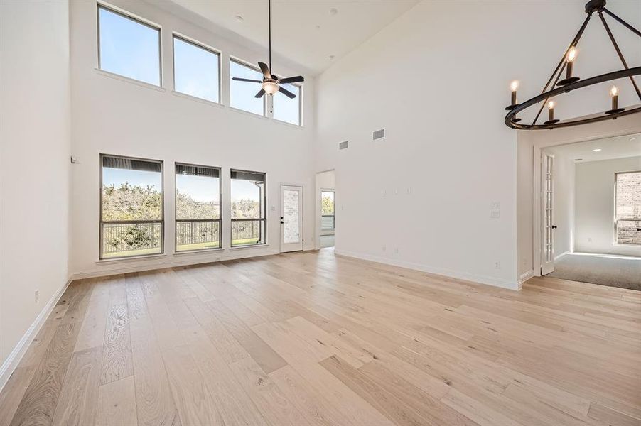 Unfurnished living room featuring ceiling fan with notable chandelier, light hardwood / wood-style flooring, and high vaulted ceiling