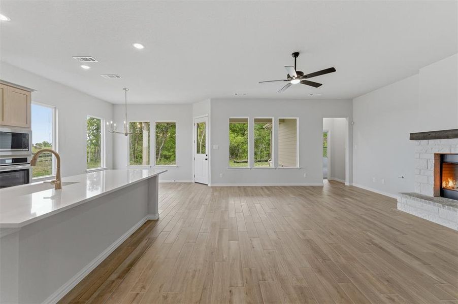 Unfurnished living room with a warm lit fireplace, light wood-style floors, healthy amount of natural light, and suspended lighting